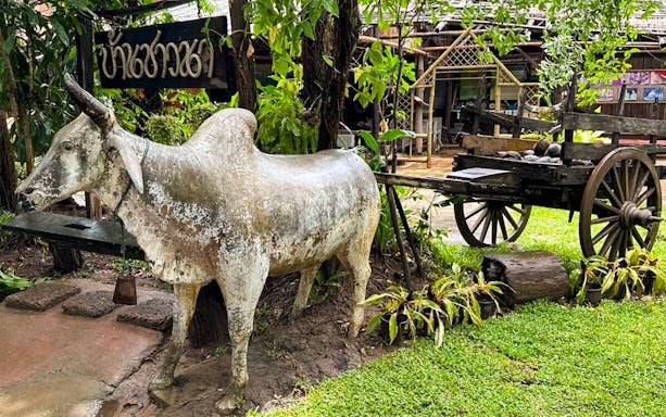Ox statue and wooden cart at a traditional Thai village on Mae Ping River cruise.