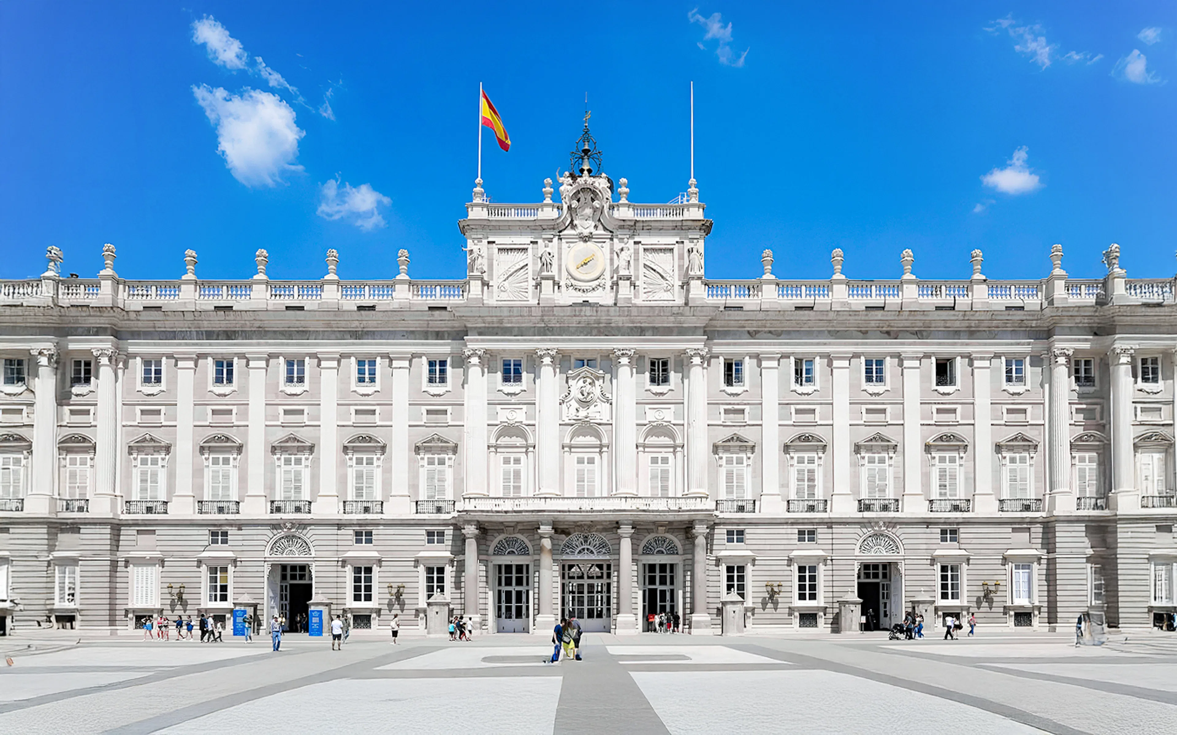 Royal Palace of Madrid facade with Spanish flag, highlighting its grand architecture.