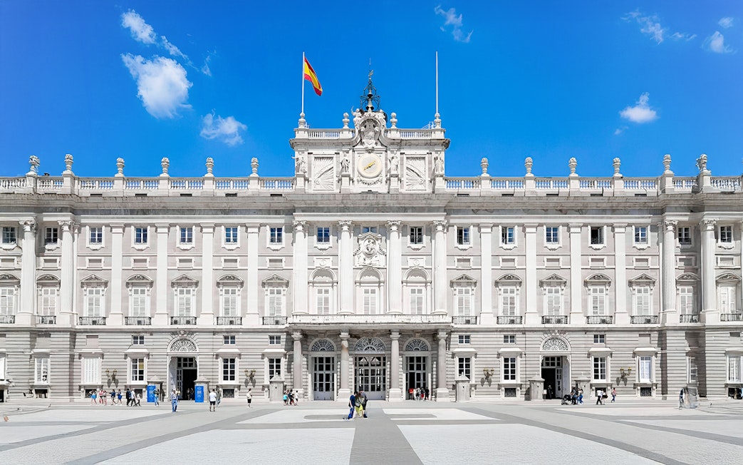 Royal Palace of Madrid facade with Spanish flag, highlighting its grand architecture.