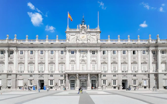 Royal Palace of Madrid facade with Spanish flag, highlighting its grand architecture.