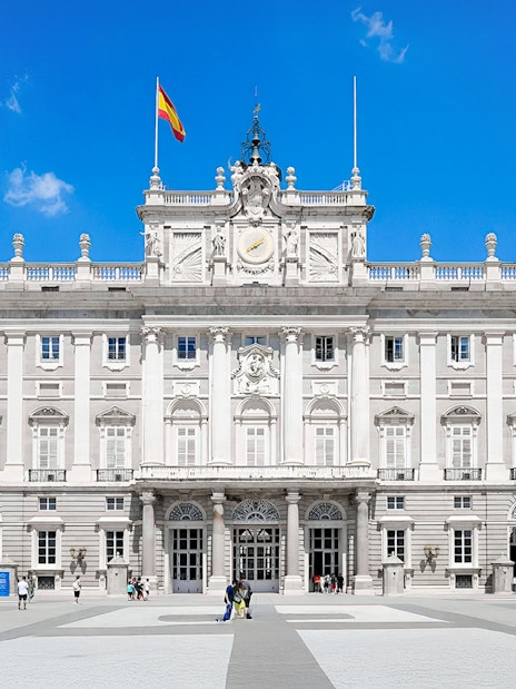Royal Palace of Madrid facade with Spanish flag, highlighting its grand architecture.