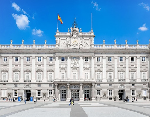 Royal Palace of Madrid facade with Spanish flag, highlighting its grand architecture.