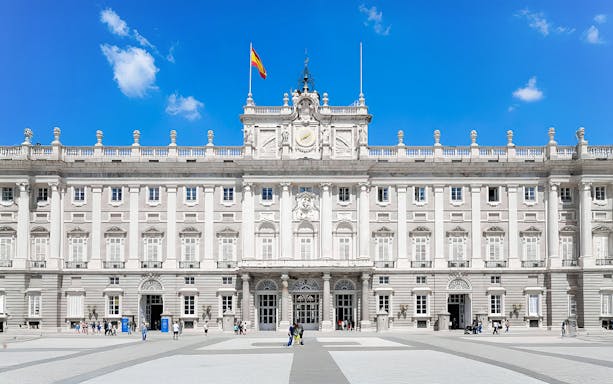 Royal Palace of Madrid facade with Spanish flag, highlighting its grand architecture.