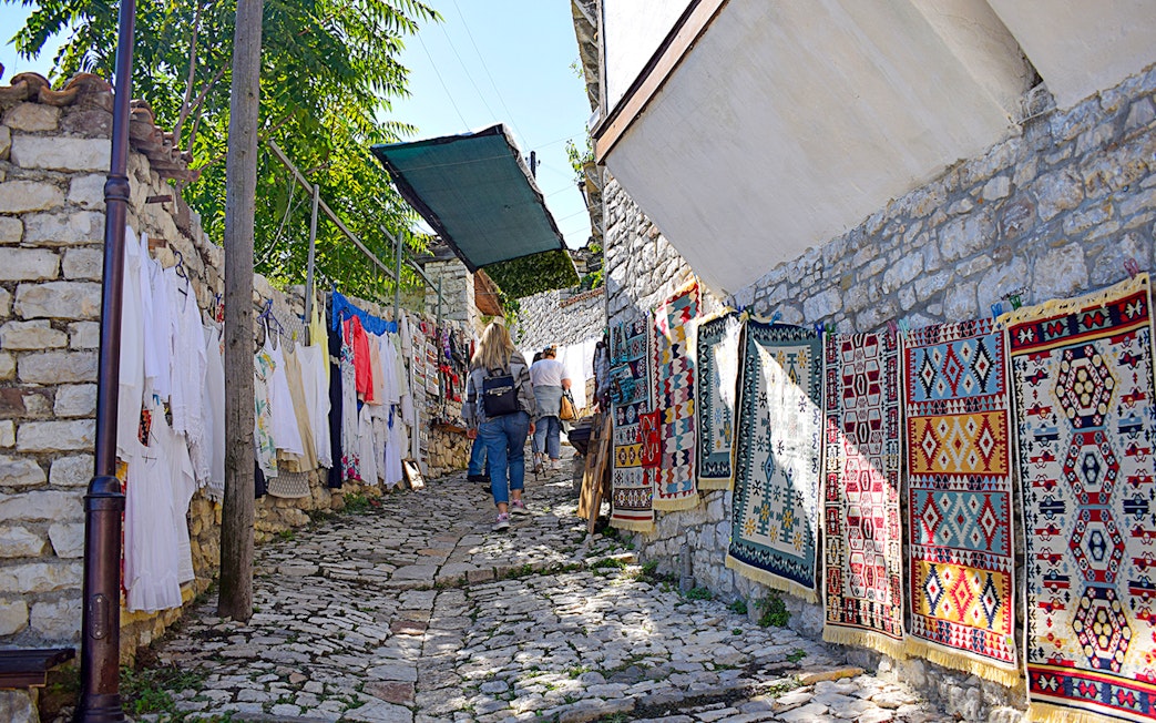 Tourist walking through cobblestone alley with colorful rugs in Berat, Albania.