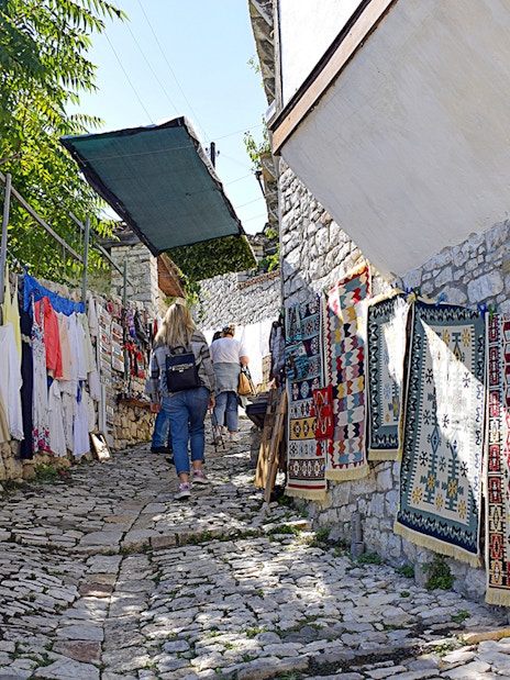 Tourist walking through cobblestone alley with colorful rugs in Berat, Albania.