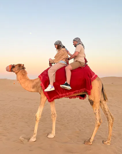Guests riding a camel in the Dubai desert at sunset.