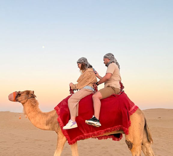 Guests riding a camel in the Dubai desert at sunset.
