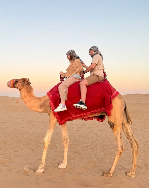 Guests riding a camel in the Dubai desert at sunset.