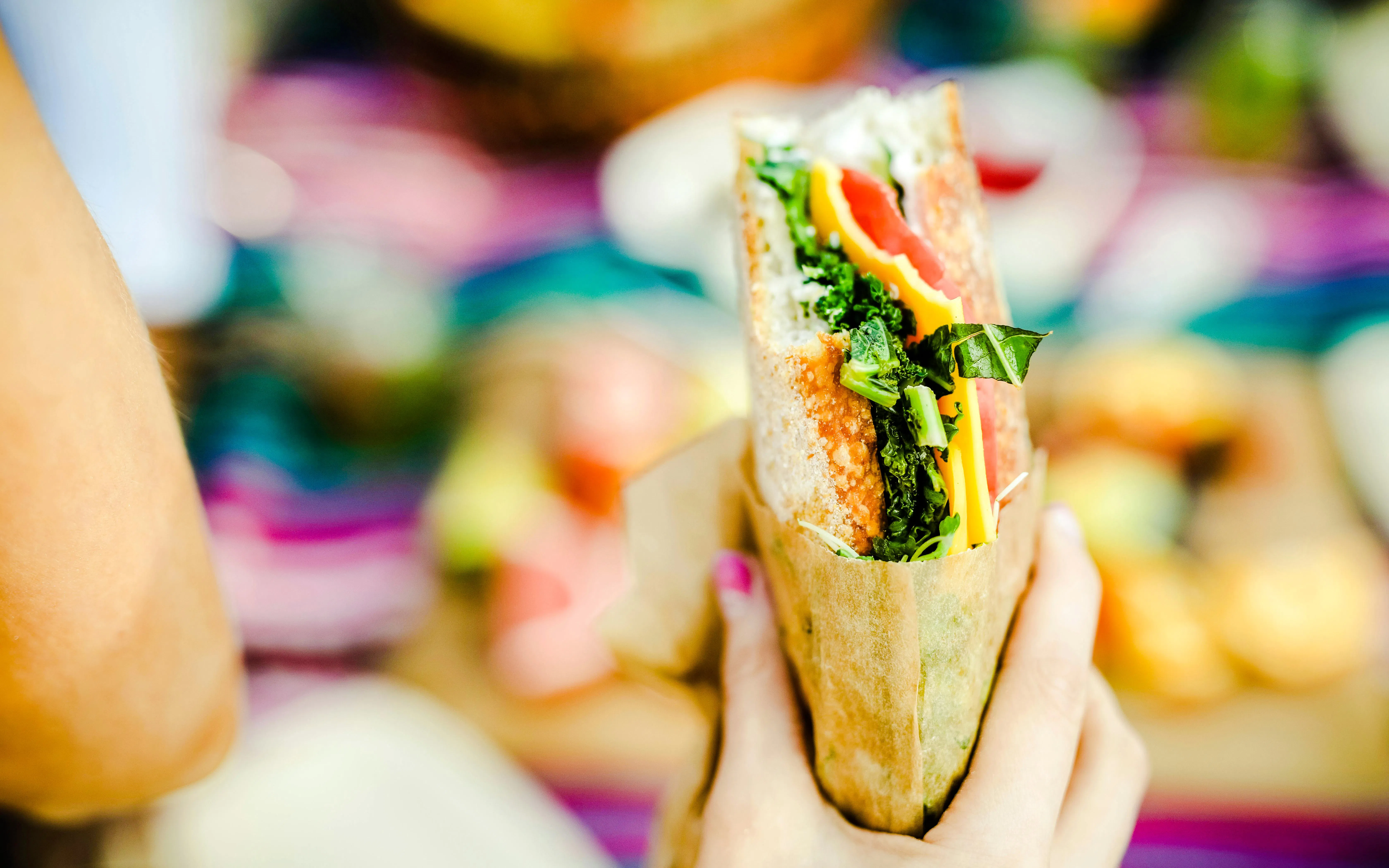 Hand holding a sandwich with greens and cheese.