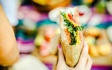 Hand holding a sandwich with greens and cheese.