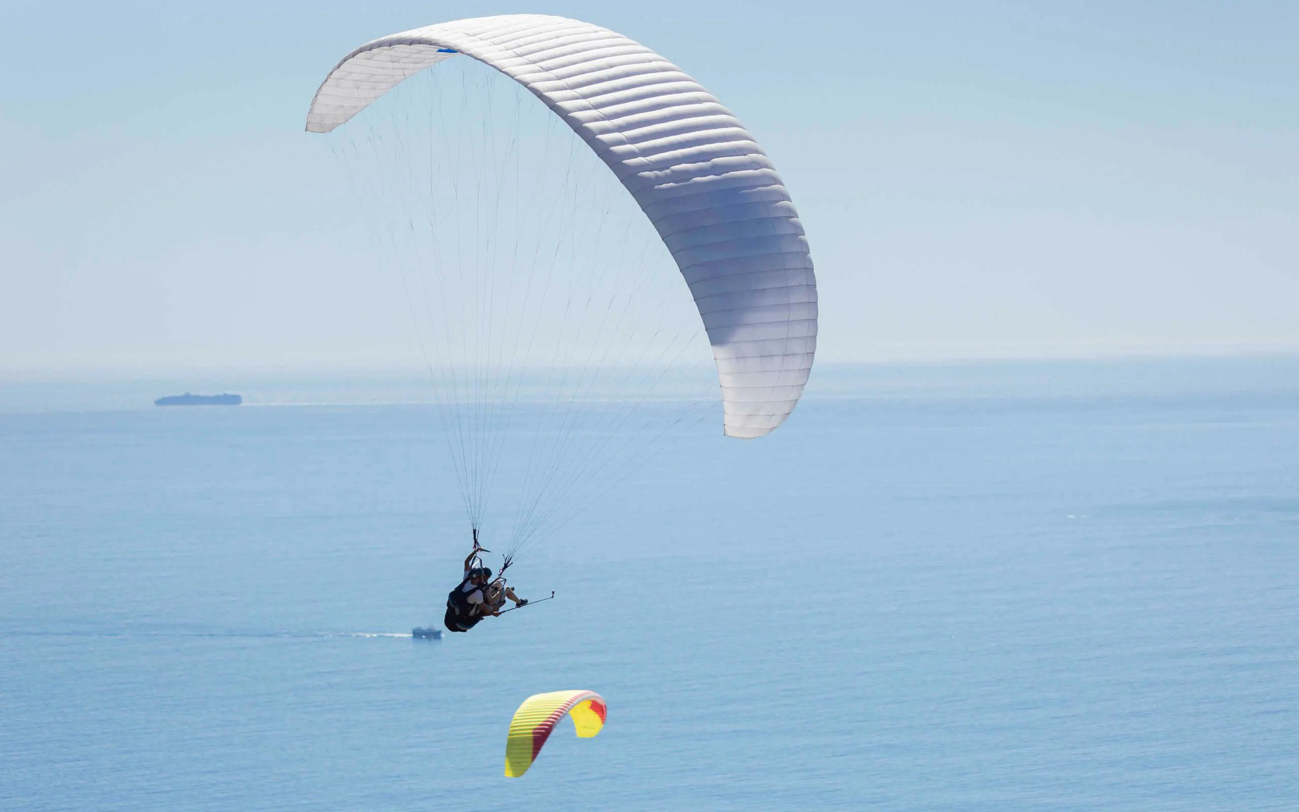 Tandem paragliding over ocean in Cape Town with distant ship.