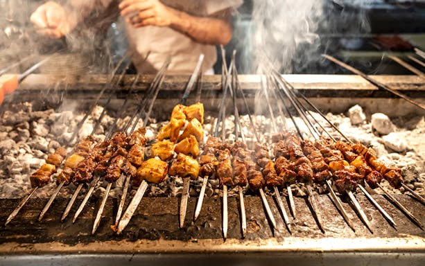 Skewers of traditional kebabs grilling over charcoal at a Turkish street food stall.