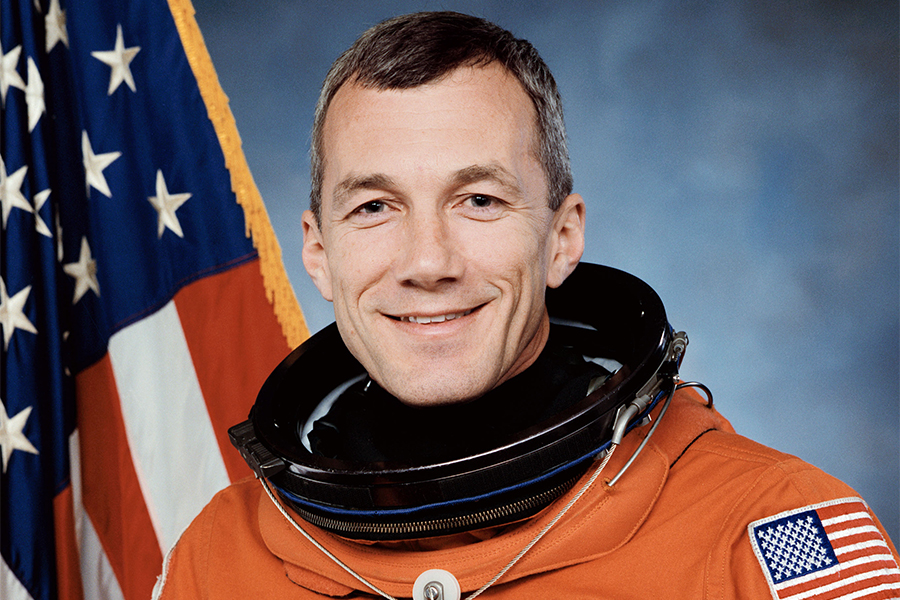 Terry Wilcutt speaking at a space exploration event in front of a NASA backdrop.