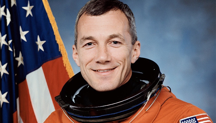 Terry Wilcutt speaking at a space exploration event in front of a NASA backdrop.