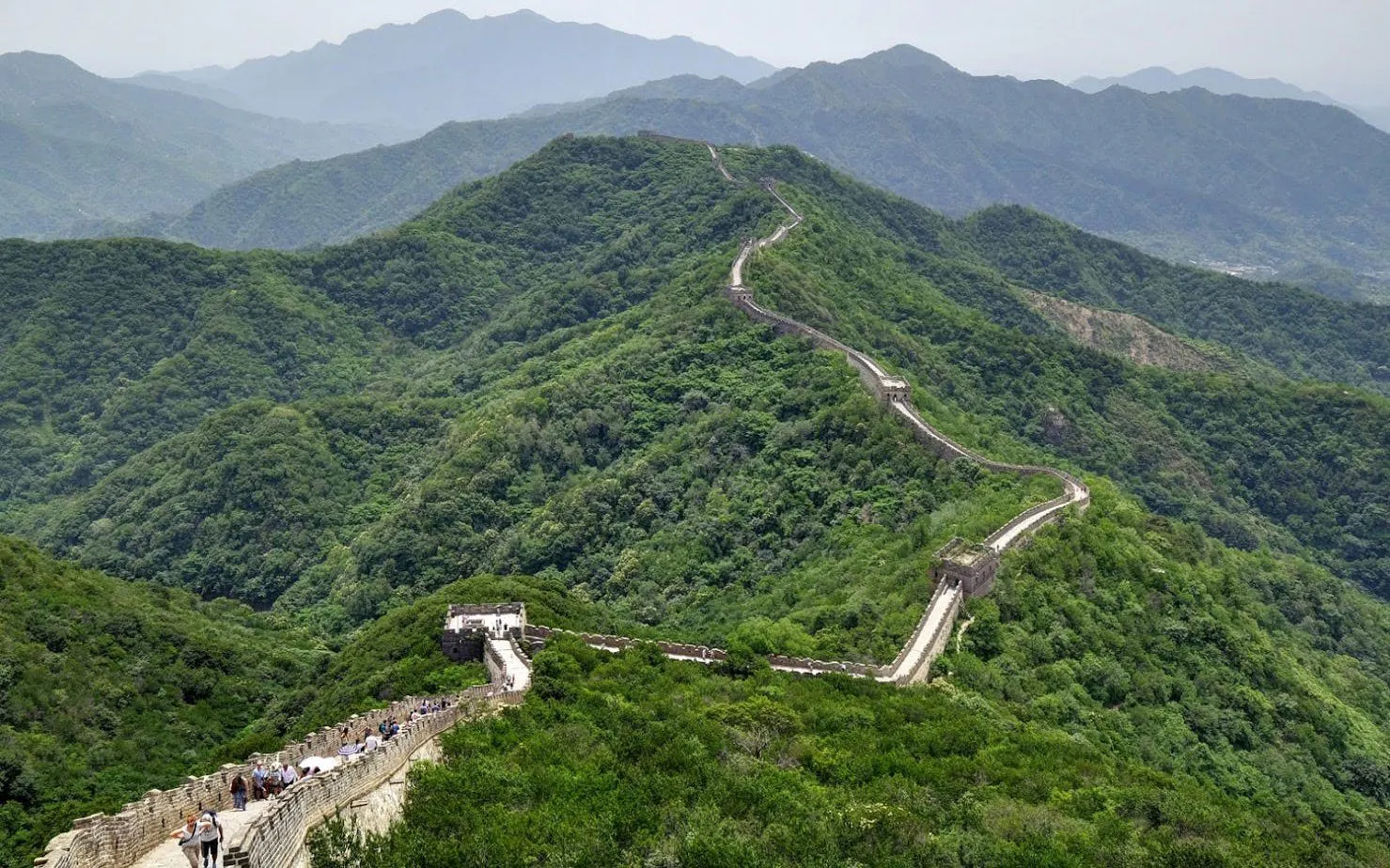 Mutianyu Great Wall winding through lush green hills, visitors walking along the path.