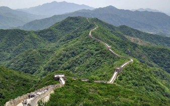 Mutianyu Great Wall winding through lush green hills, visitors walking along the path.