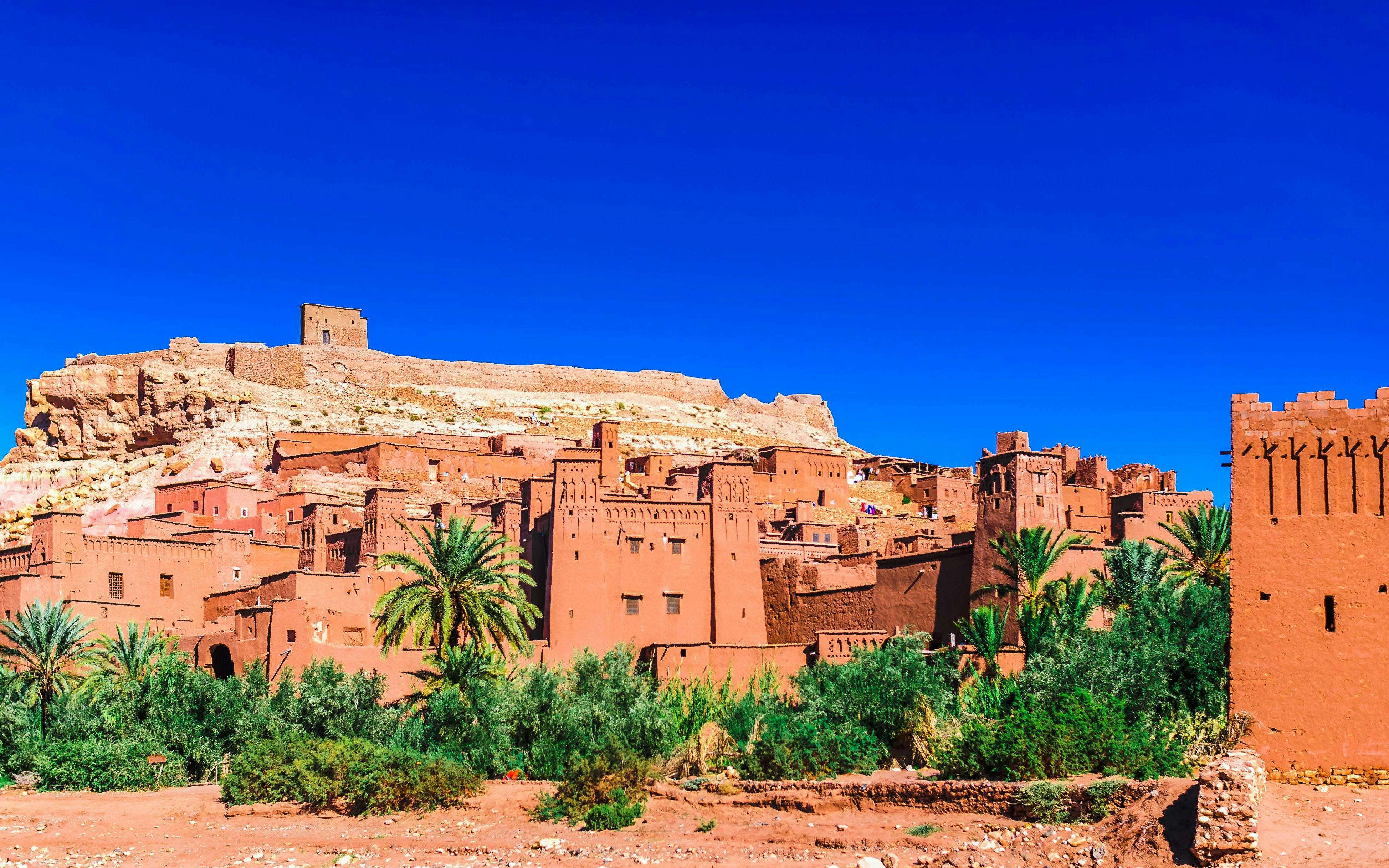 Ait Ben Haddou kasbah with clay buildings and palm trees in Morocco.