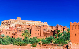 Ait Ben Haddou kasbah with clay buildings and palm trees in Morocco.