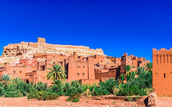 Ait Ben Haddou kasbah with clay buildings and palm trees in Morocco.