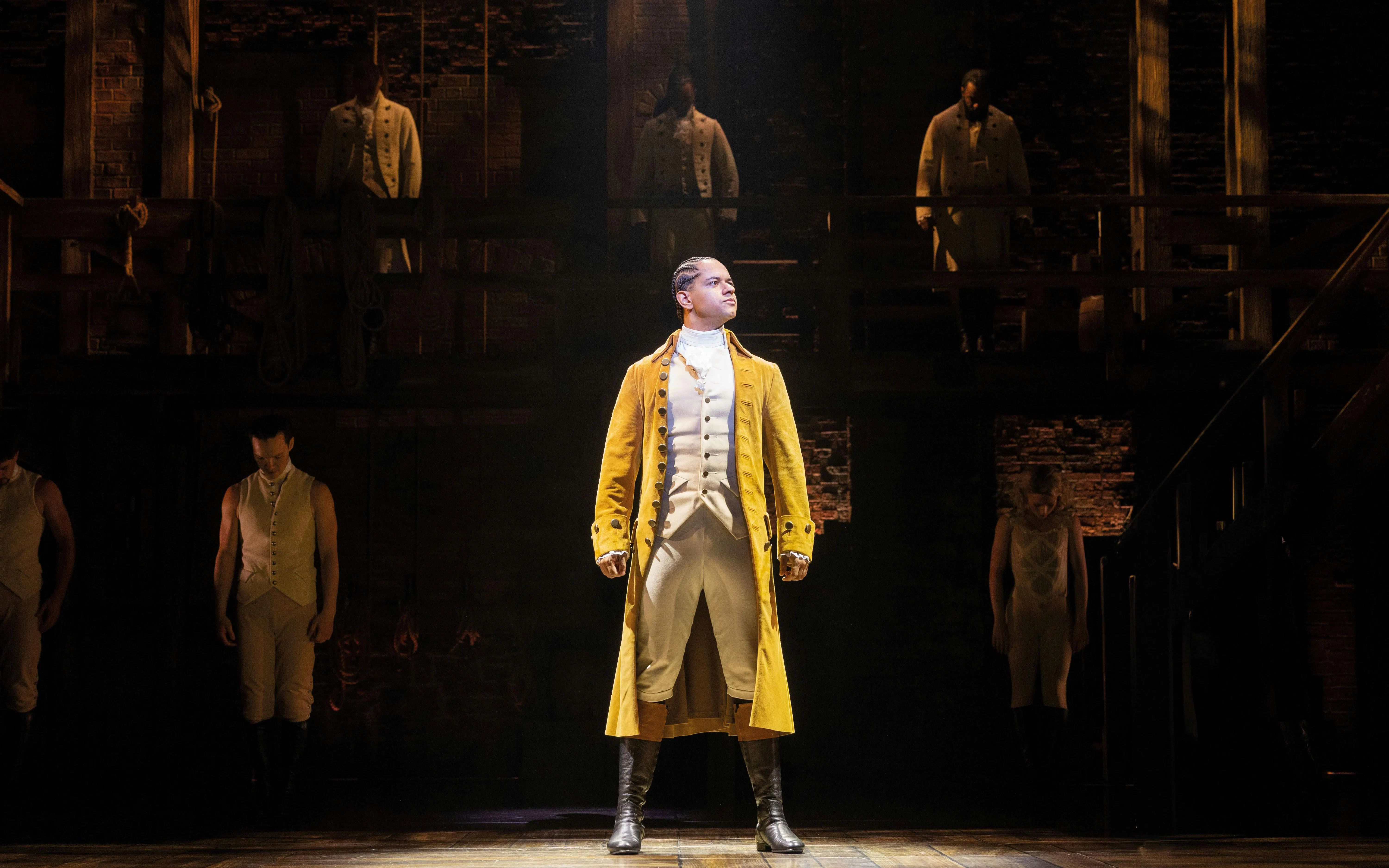 Hamilton West End performance with lead actor in yellow coat on stage.