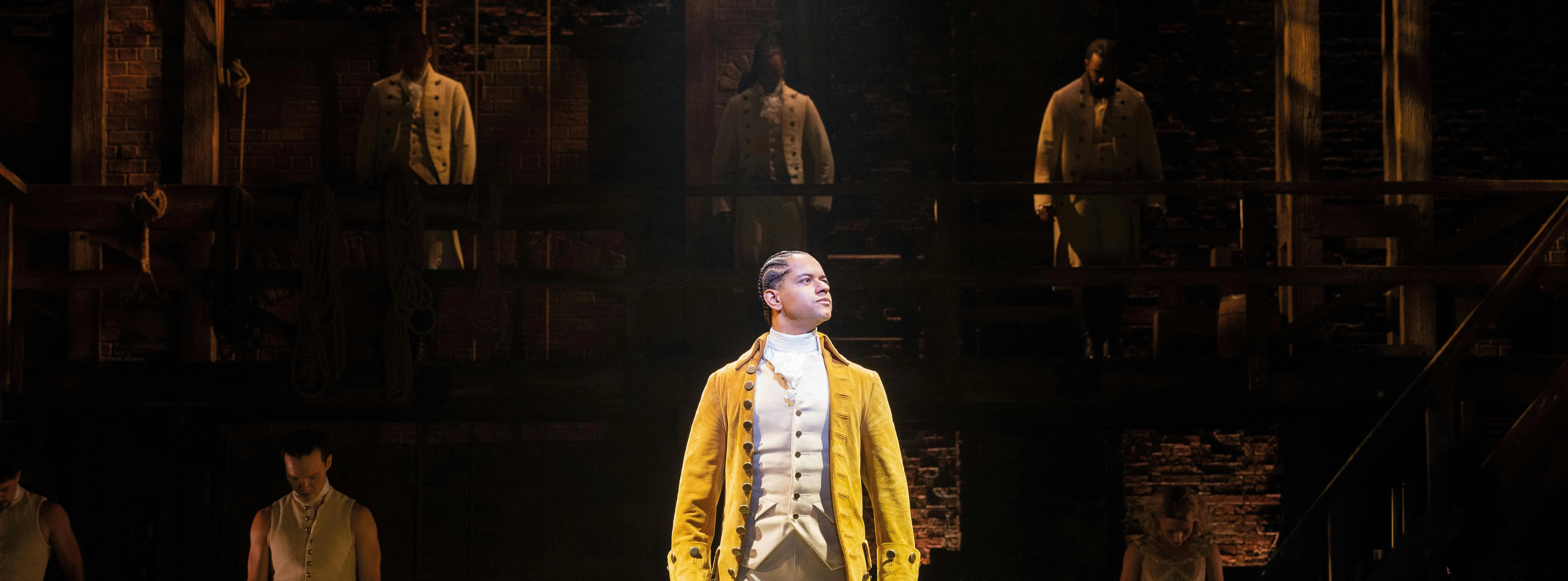 Hamilton West End performance with lead actor in yellow coat on stage.