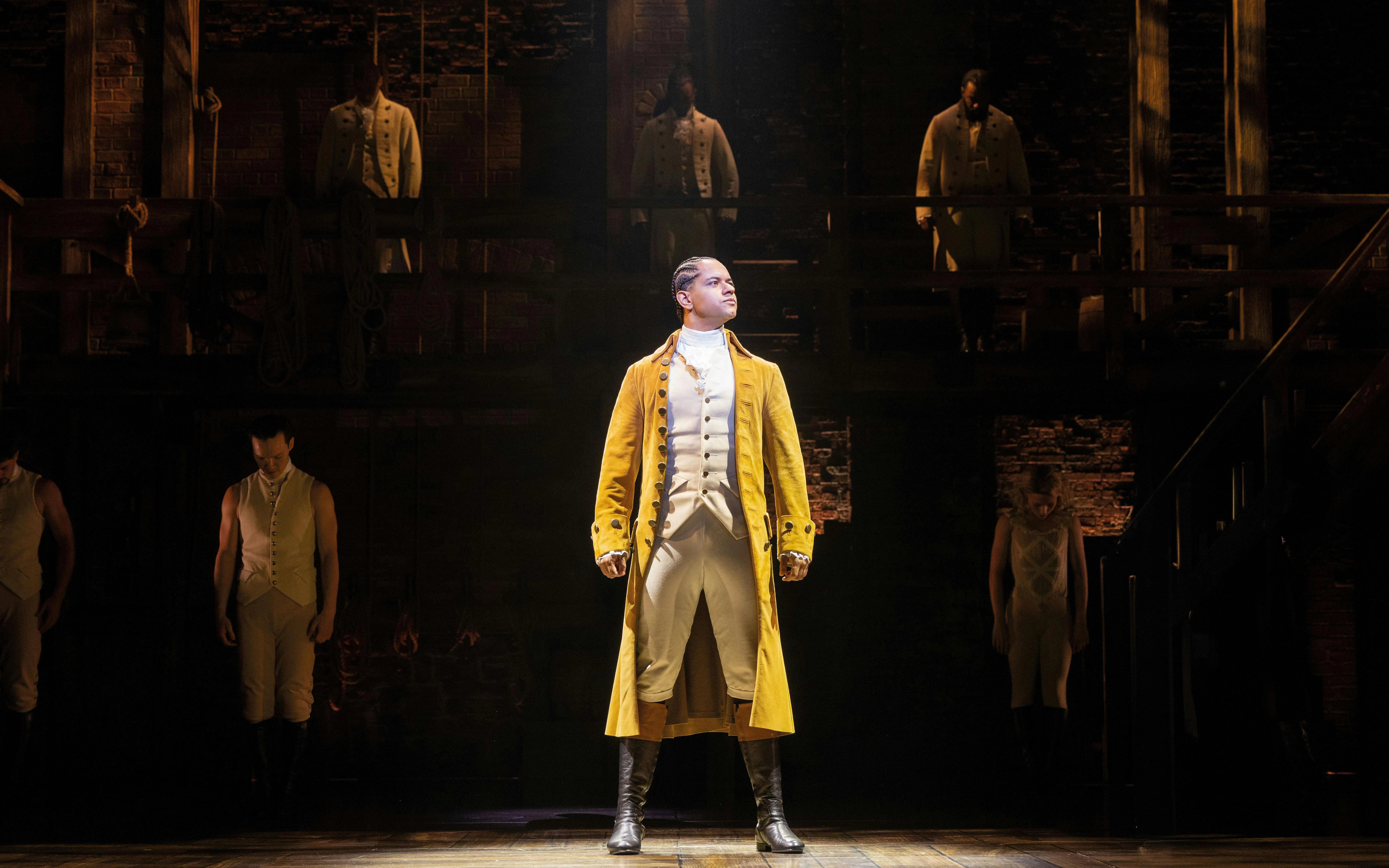 Hamilton West End performance with lead actor in yellow coat on stage.