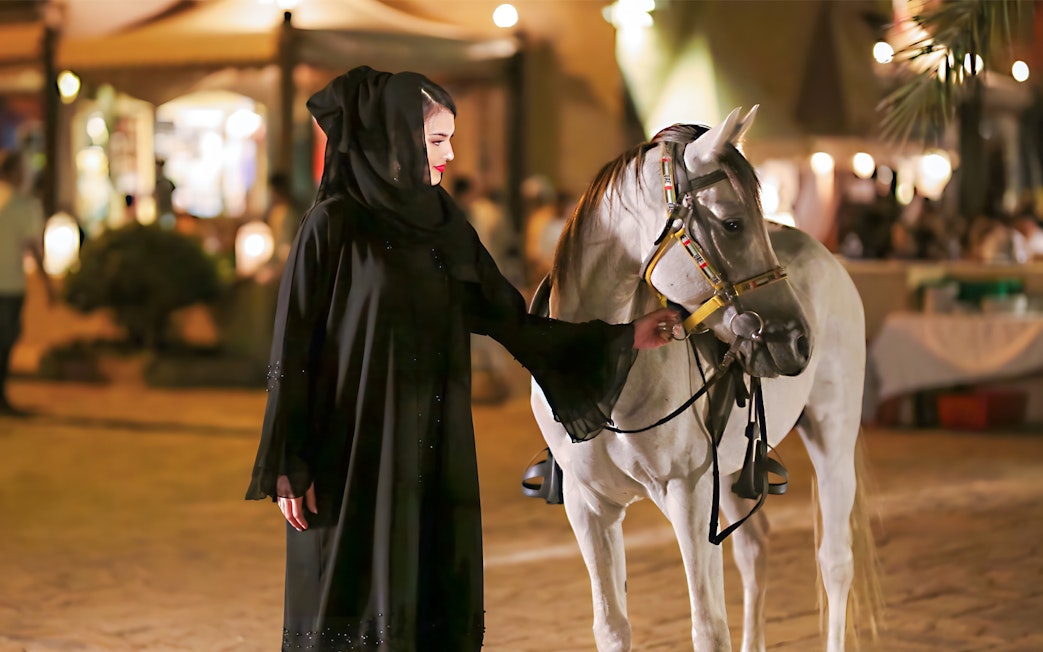 Woman in traditional attire with a horse at a Dubai royal dinner event.