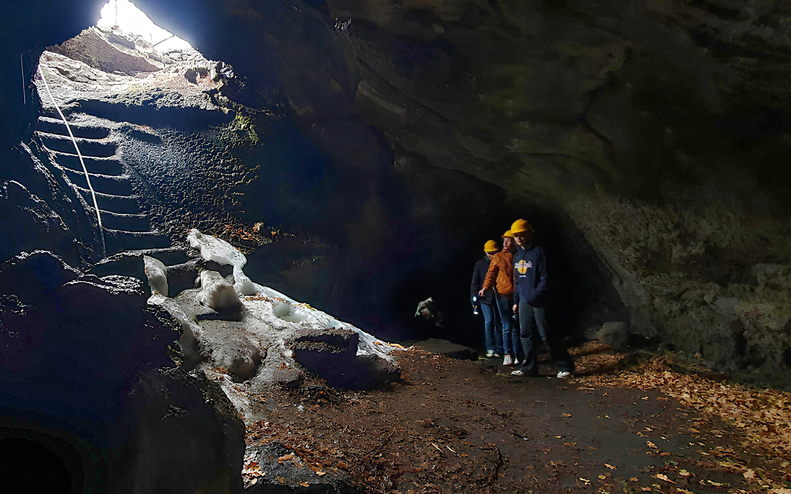 Tourists with a guide exploring a lava cave with icy formations and a stone staircase.
