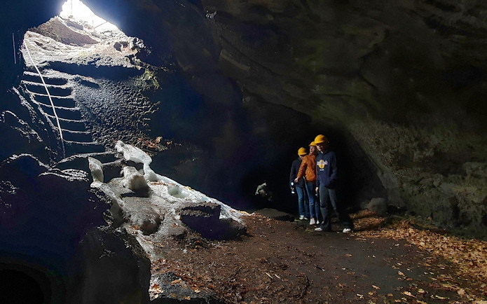 Tourists with a guide exploring a lava cave with icy formations and a stone staircase.
