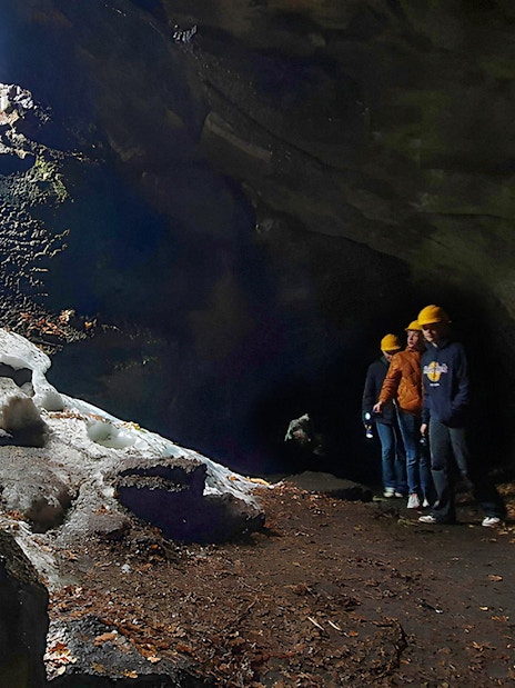 Tourists with a guide exploring a lava cave with icy formations and a stone staircase.