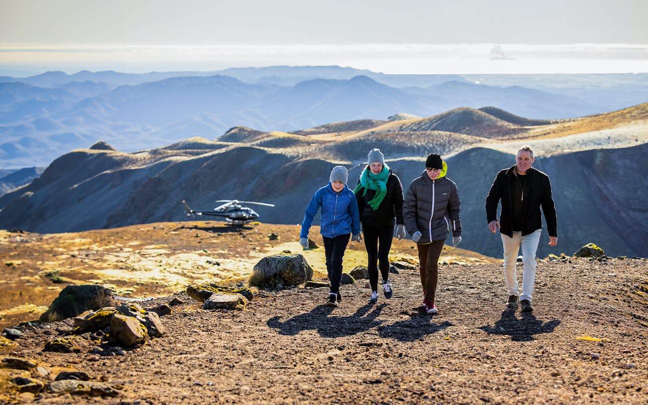 Visitors walking on Mount Tarawera with a helicopter in the background, New Zealand.
