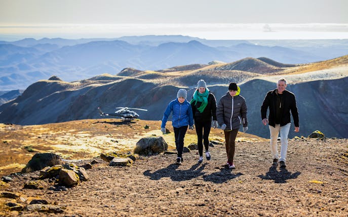 Visitors walking on Mount Tarawera with a helicopter in the background, New Zealand.