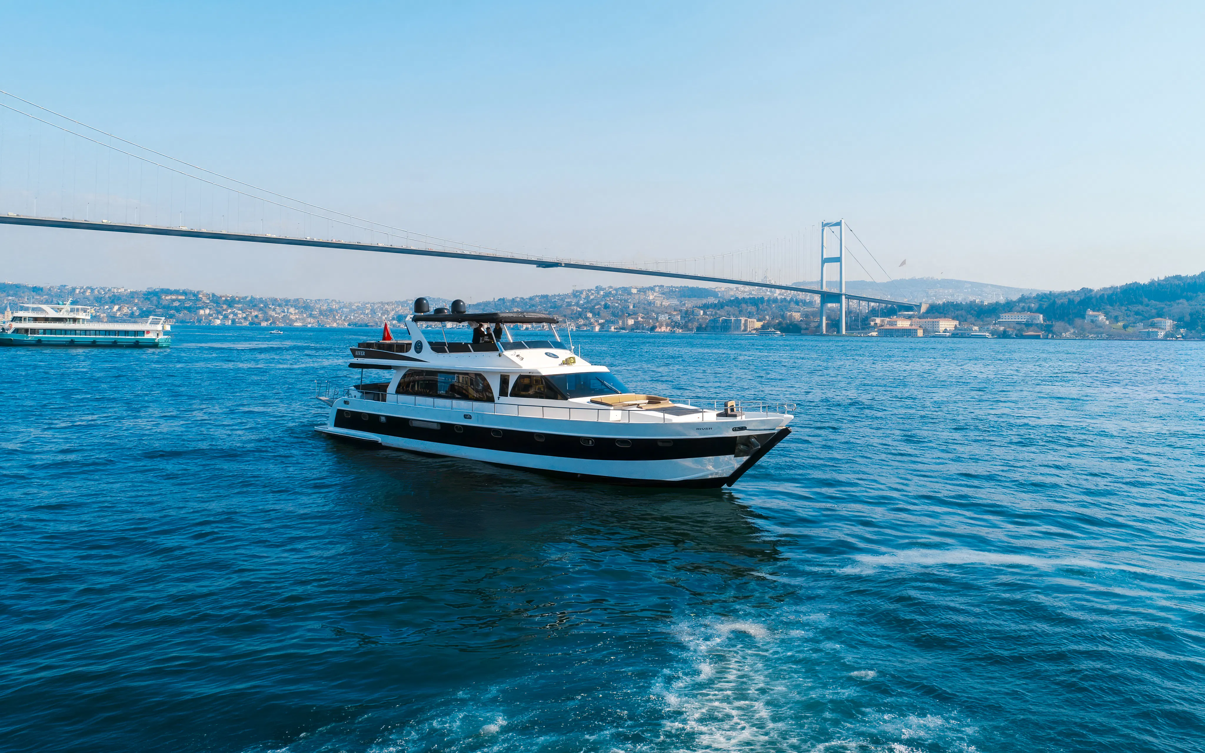 Luxury yacht cruising on the Bosphorus with Istanbul's skyline and bridge in the background.