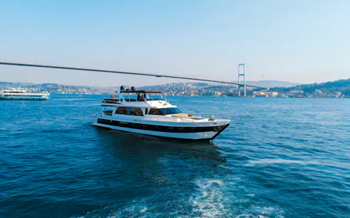 Luxury yacht cruising on the Bosphorus with Istanbul's skyline and bridge in the background.