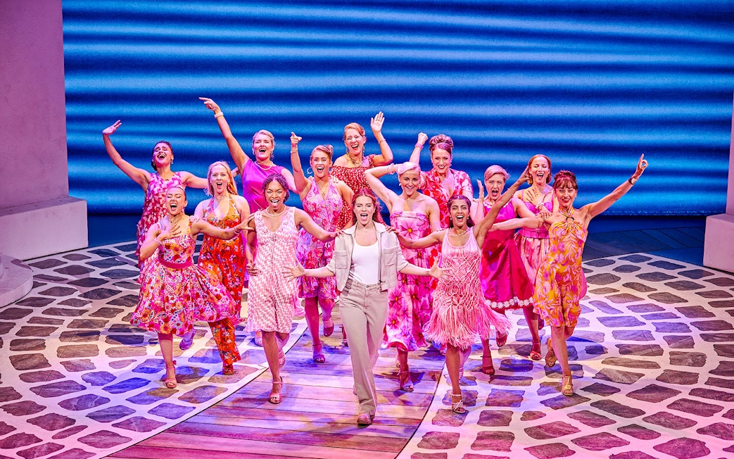Performers in colorful costumes singing and dancing in a Mamma Mia production.