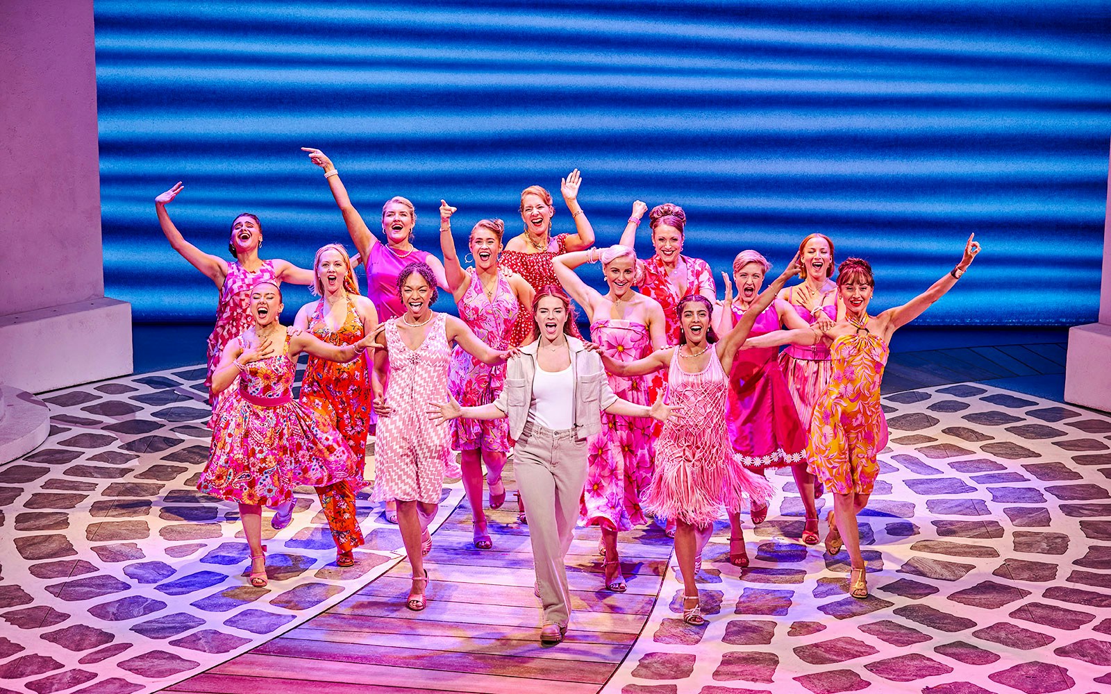 Performers in colorful costumes singing and dancing in a Mamma Mia production.