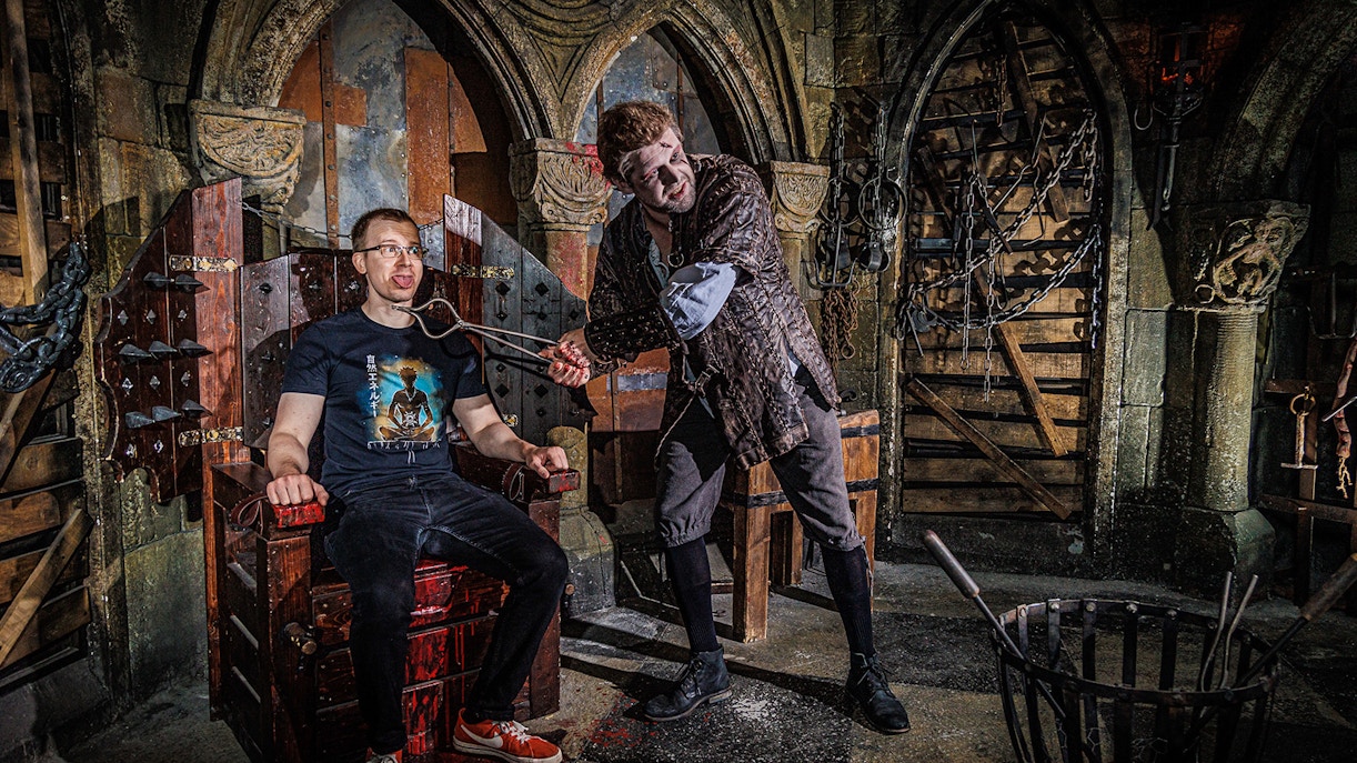 Torturer interacting with a visitor at the Berlin Dungeon in a medieval-themed setting.