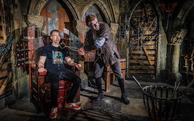Torturer interacting with a visitor at the Berlin Dungeon in a medieval-themed setting.