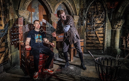 Torturer interacting with a visitor at the Berlin Dungeon in a medieval-themed setting.