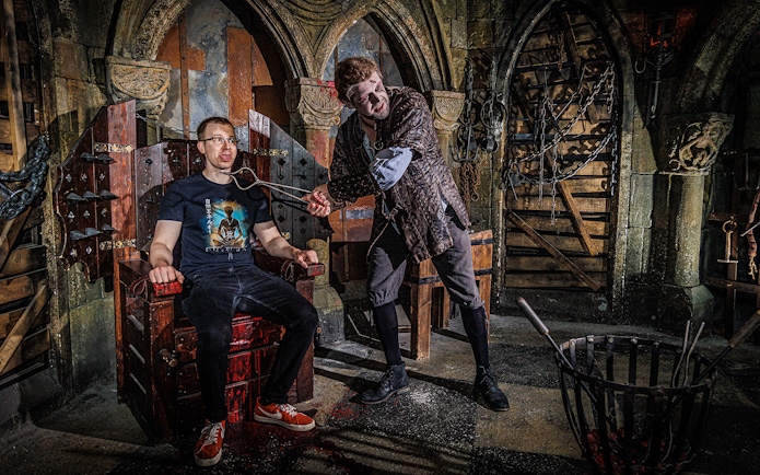Torturer interacting with a visitor at the Berlin Dungeon in a medieval-themed setting.