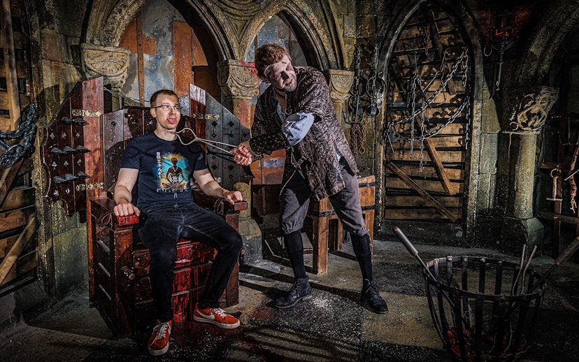 Torturer interacting with a visitor at the Berlin Dungeon in a medieval-themed setting.
