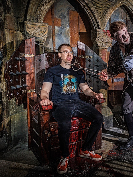 Torturer interacting with a visitor at the Berlin Dungeon in a medieval-themed setting.