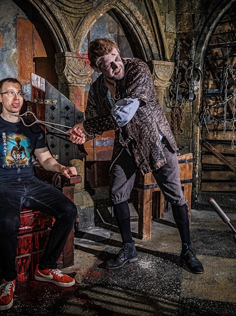 Torturer interacting with a visitor at the Berlin Dungeon in a medieval-themed setting.