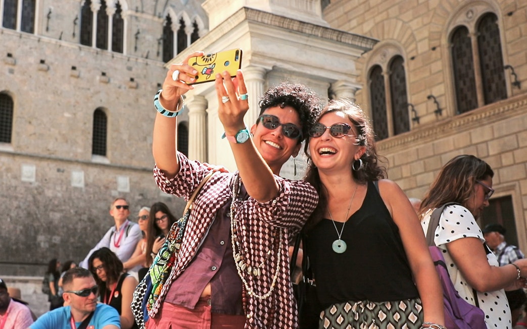 Tourists taking a selfie in front of a historic building in Siena, Italy.