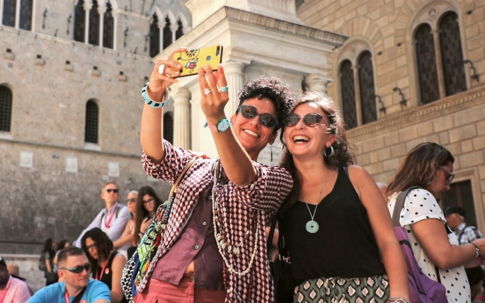 Tourists taking a selfie in front of a historic building in Siena, Italy.