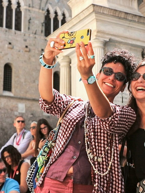 Tourists taking a selfie in front of a historic building in Siena, Italy.