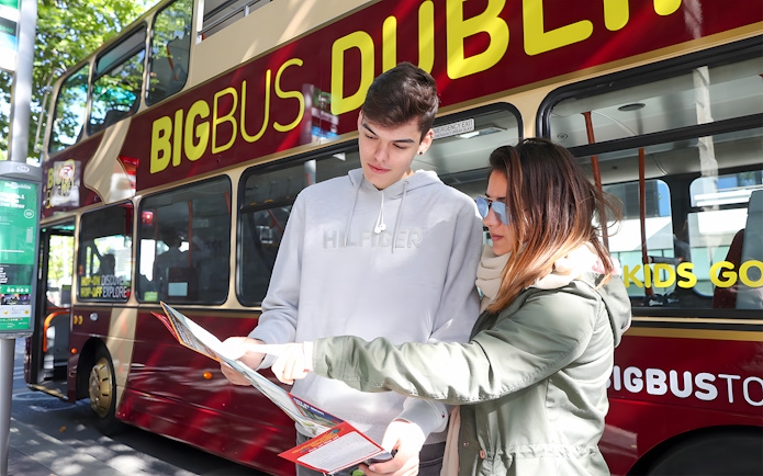 Couple examining hop-on hop-off bus route map in front of Dublin tour bus.
