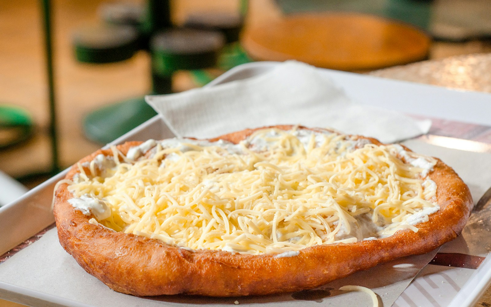 Traditional Hungarian Lángos topped with cheese on a tray.