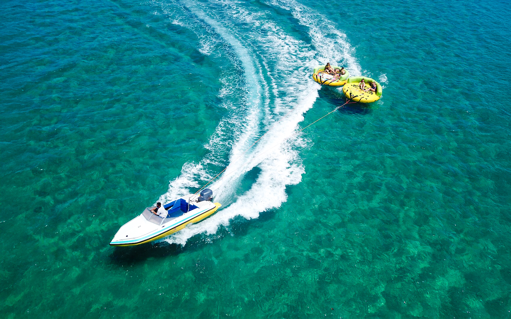 Aerial view of a speedboat towing a donut ride on turquoise waters in Dubai.