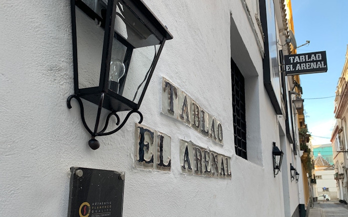 Tablao El Arenal entrance sign on a white building wall in Seville.